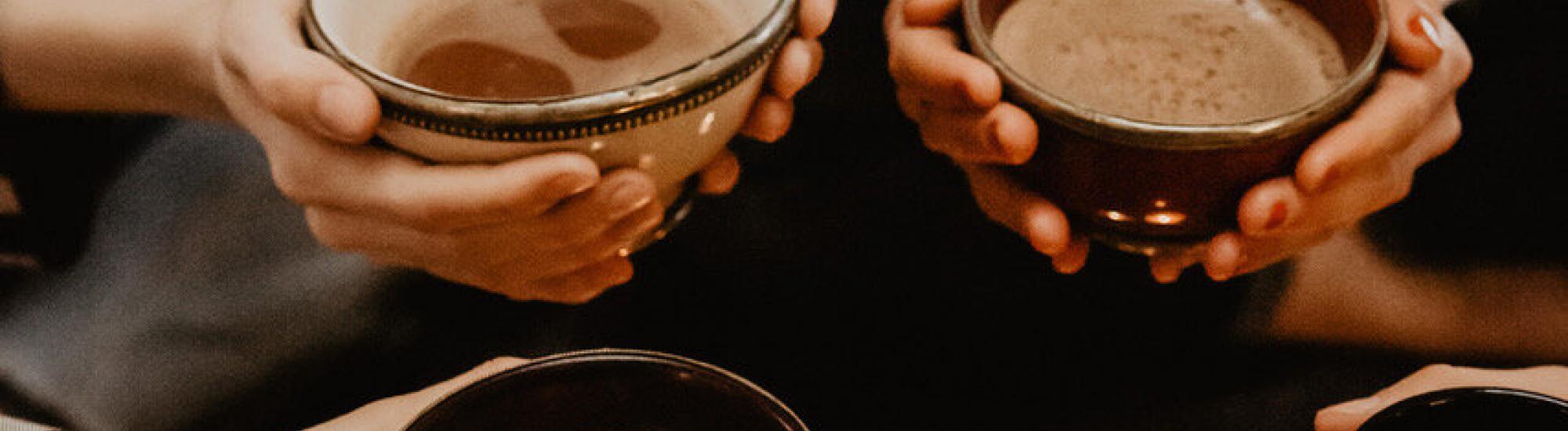hands holding mugs of cacao